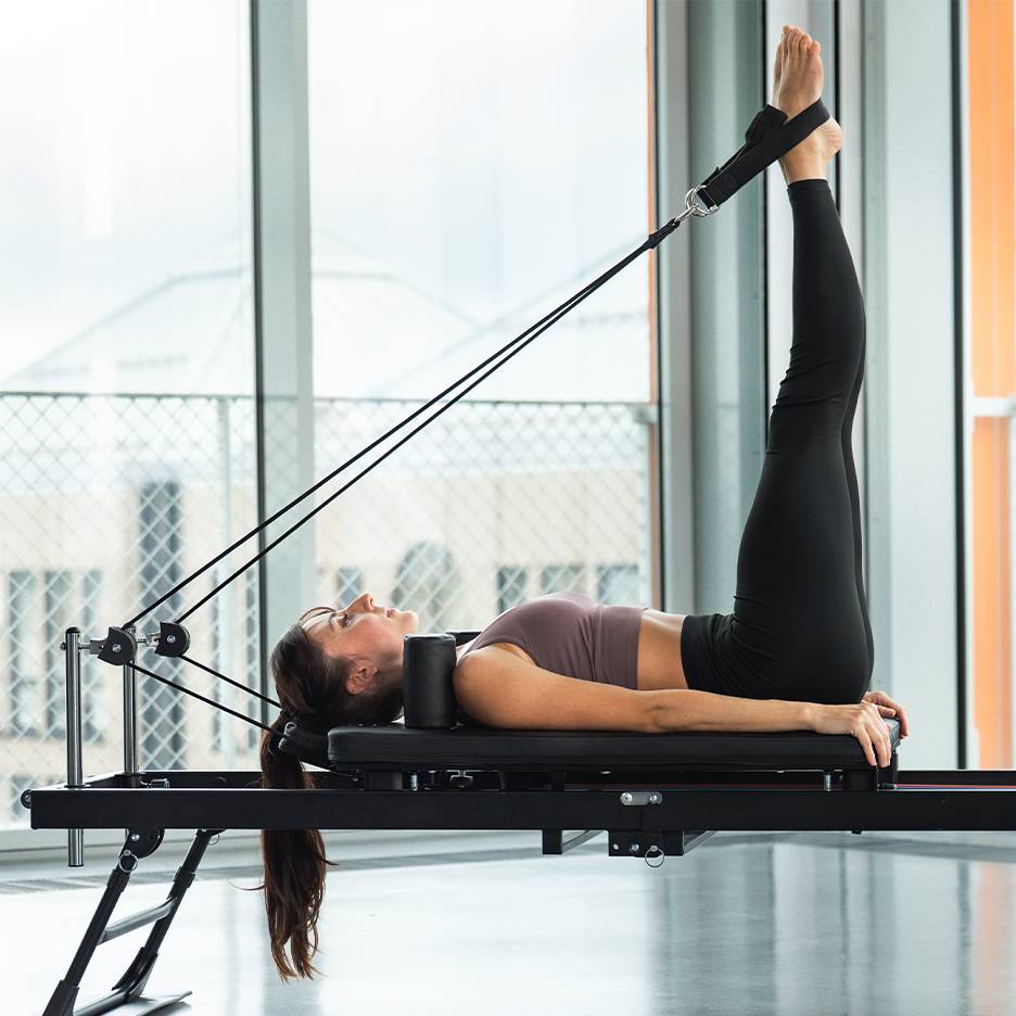 Γυναίκα κάνει άσκηση ποδιών σε μηχάνημα pilates reformer.