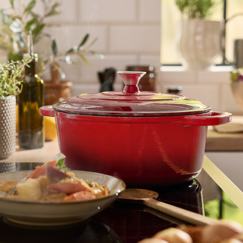 Μια κόκκινη χυτοσιδηρή κατσαρόλα σε εστία, με ένα μπολ μαγειρεμένου φαγητού δίπλα.