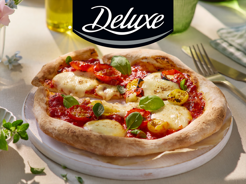 Μια πίτσα Deluxe με ντομάτες και μοτσαρέλα σε ξύλινη βάση.