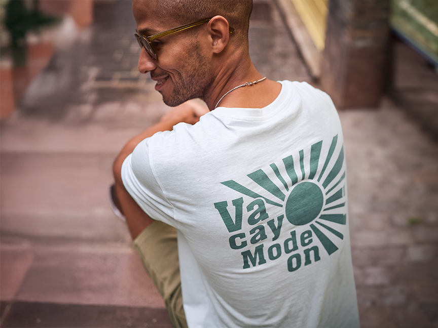 Ένα άτομο φοράει ένα λευκό t-shirt με την επιγραφή 'Vacay Mode On'.