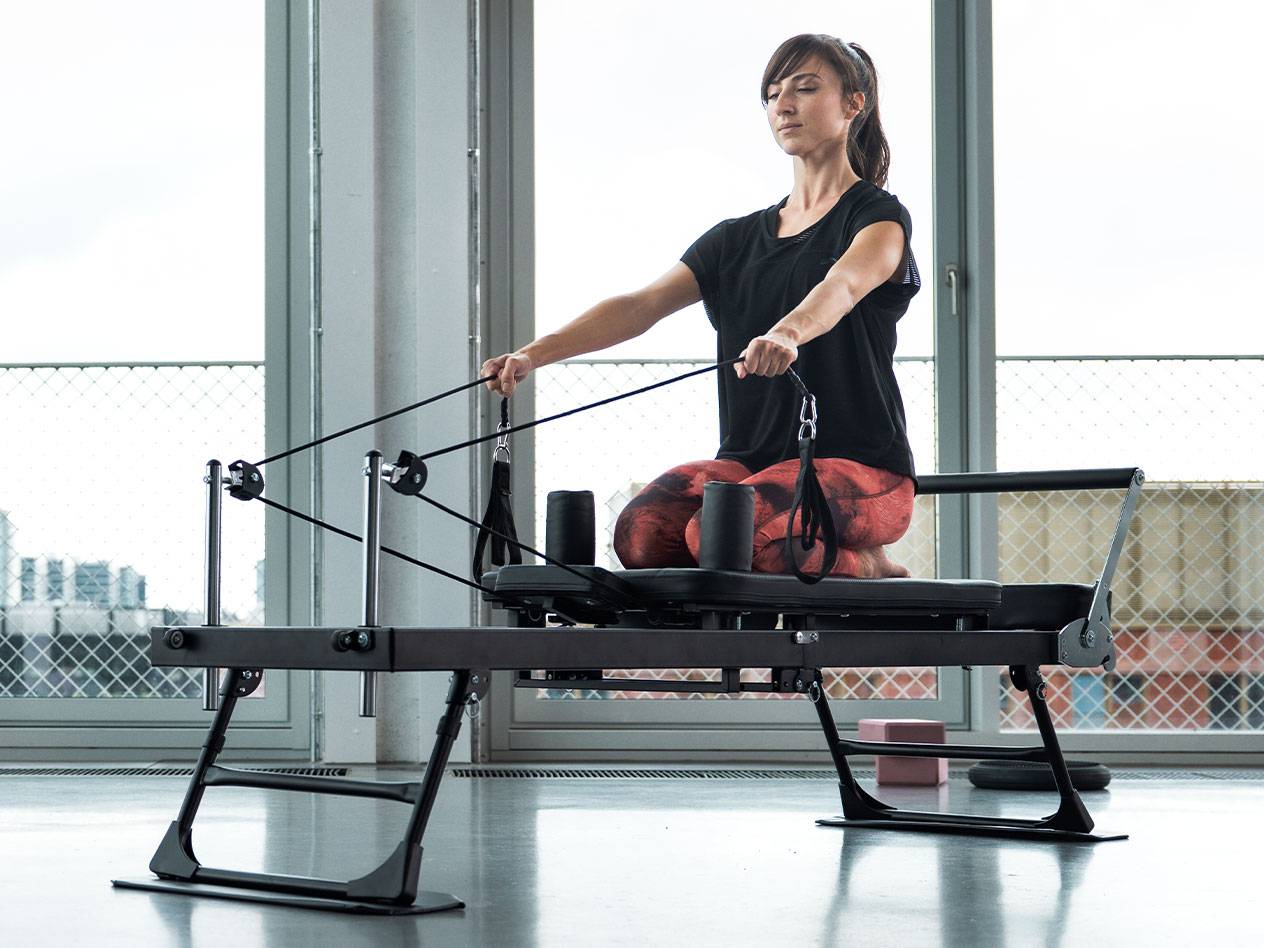 Γυναίκα κάνει Pilates σε reformer με μεγάλα παράθυρα στο παρασκήνιο.