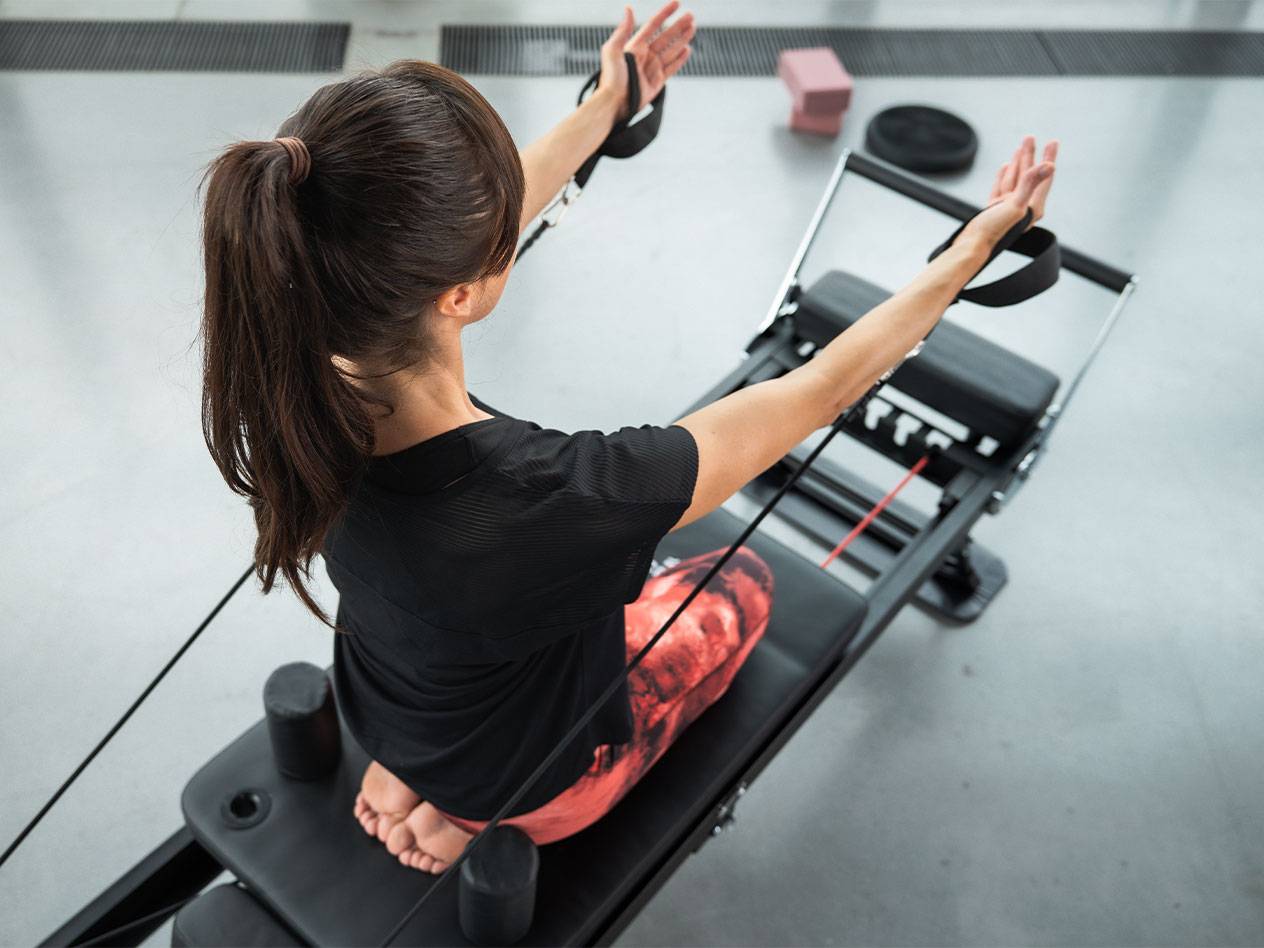 Γυναίκα κάνει Pilates σε μηχάνημα reformer με λάστιχα αντίστασης.