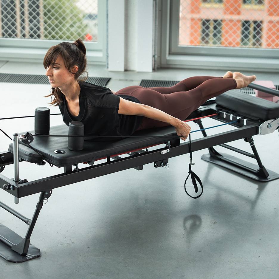 Γυναίκα ασκείται σε μηχάνημα Pilates με ελαστικούς ιμάντες.