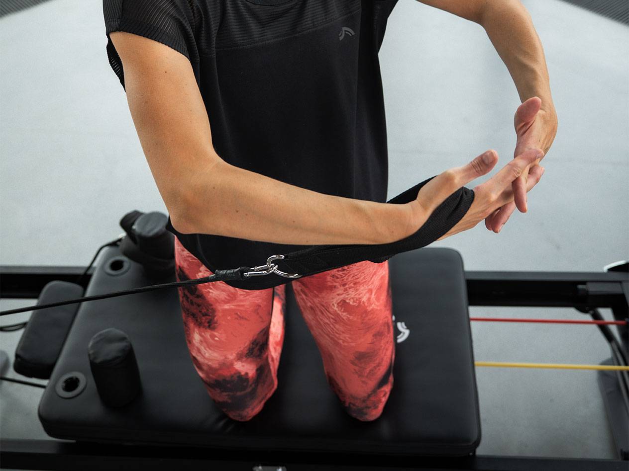 Γυναίκα ασκείται με λάστιχα αντίστασης σε μηχάνημα Pilates.