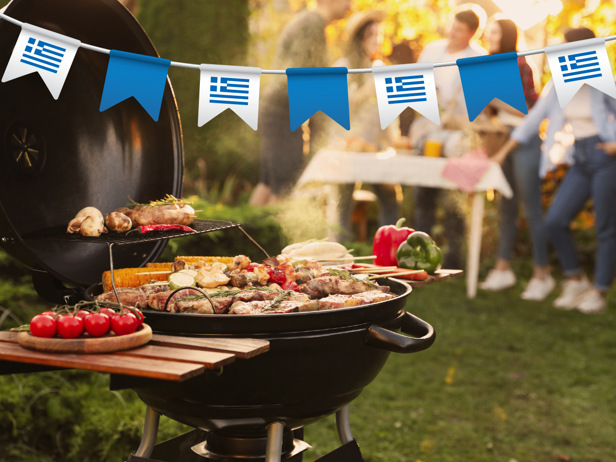 Μια ψησταριά γεμάτη κρέας και λαχανικά, με σημαίες της Ελλάδας στο φόντο.