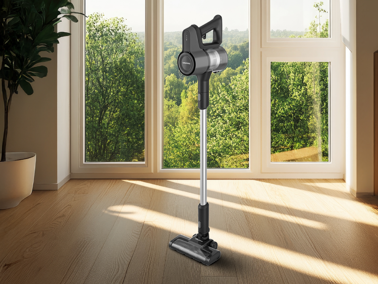 Μια ηλεκτρική σκούπα GRUNDIG® Σκούπα stick  επαναφορτιζόμενη 2 σε 1 VCP 4330 L στέκεται σε ξύλινο δάπεδο μπροστά σε ένα παράθυρο.
