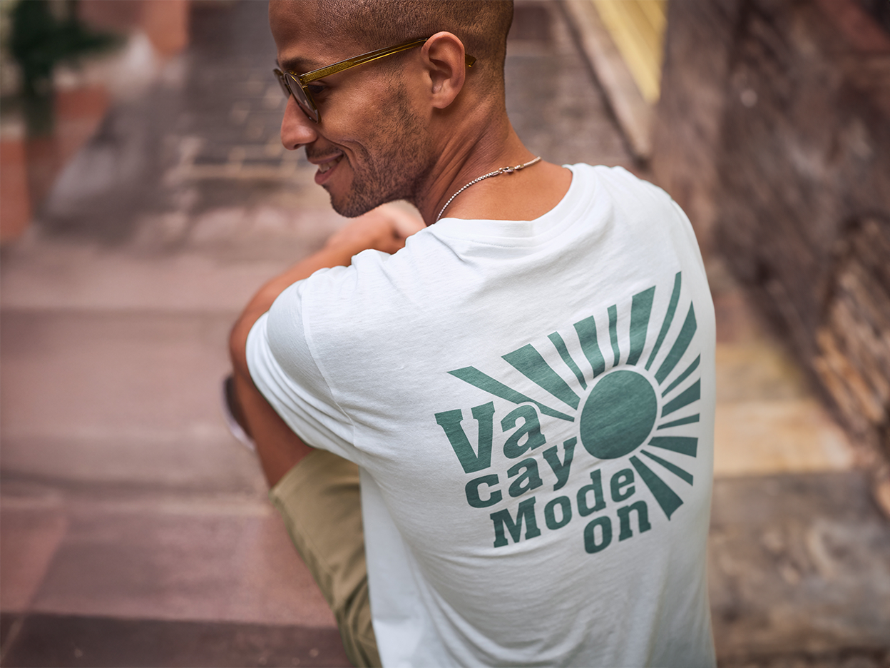 Ένας άντρας φοράει ένα λευκό t-shirt με την επιγραφή 'Vacay Mode On' και χαμογελάει.