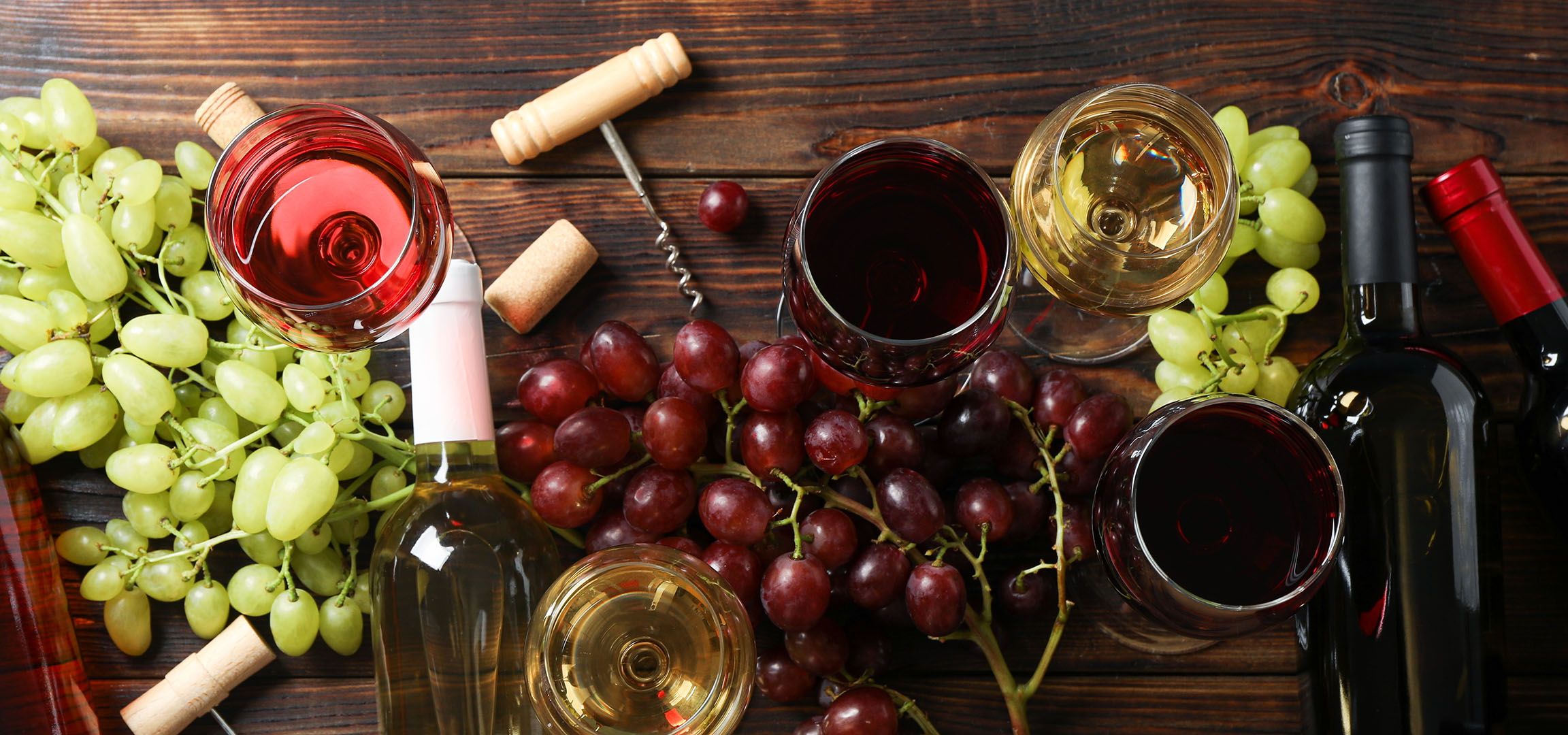 Διάφορα κρασιά, σταφύλια και αξεσουάρ κρασιού σε ξύλινο τραπέζι.