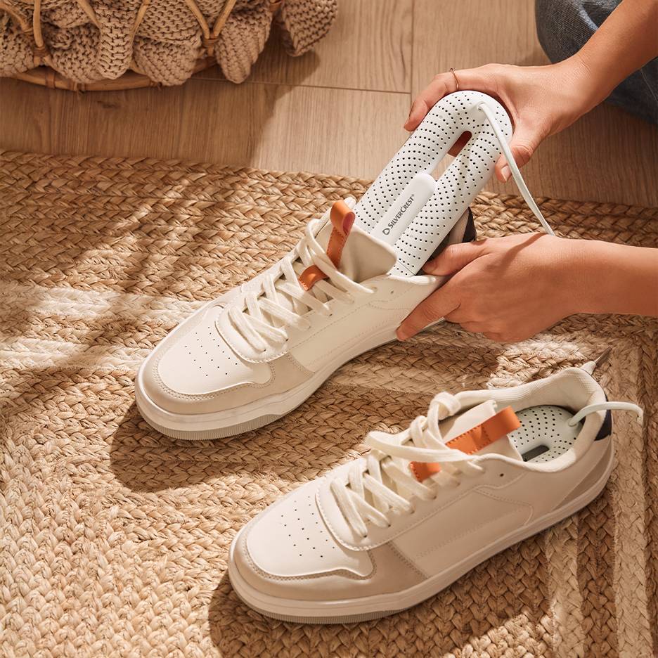 Στεγνωτήρας παπουτσιών Silvercrest σε λευκά αθλητικά παπούτσια σε πλεκτό χαλί.