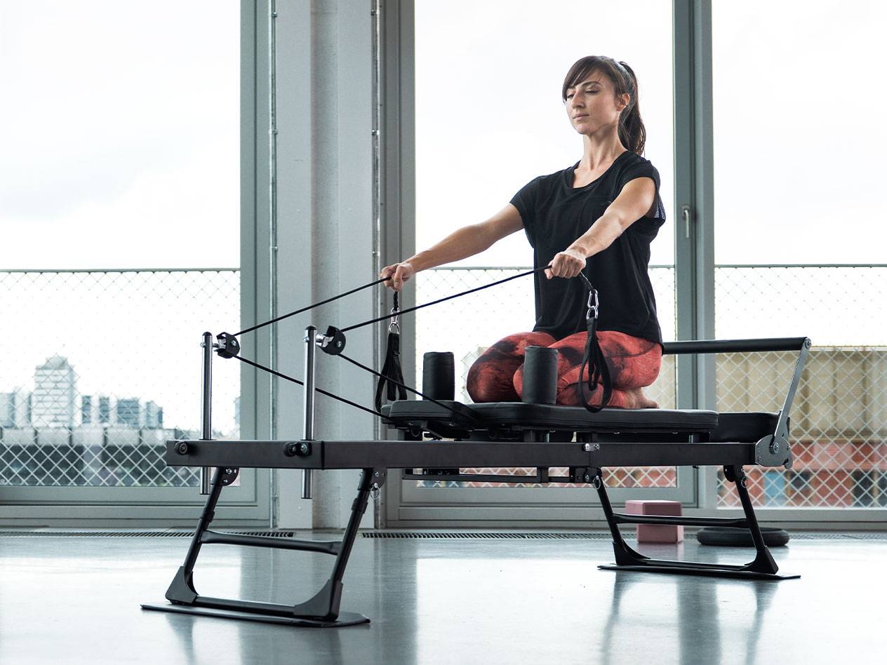 Γυναίκα κάνει Pilates σε μηχάνημα reformer με φόντο την πόλη.