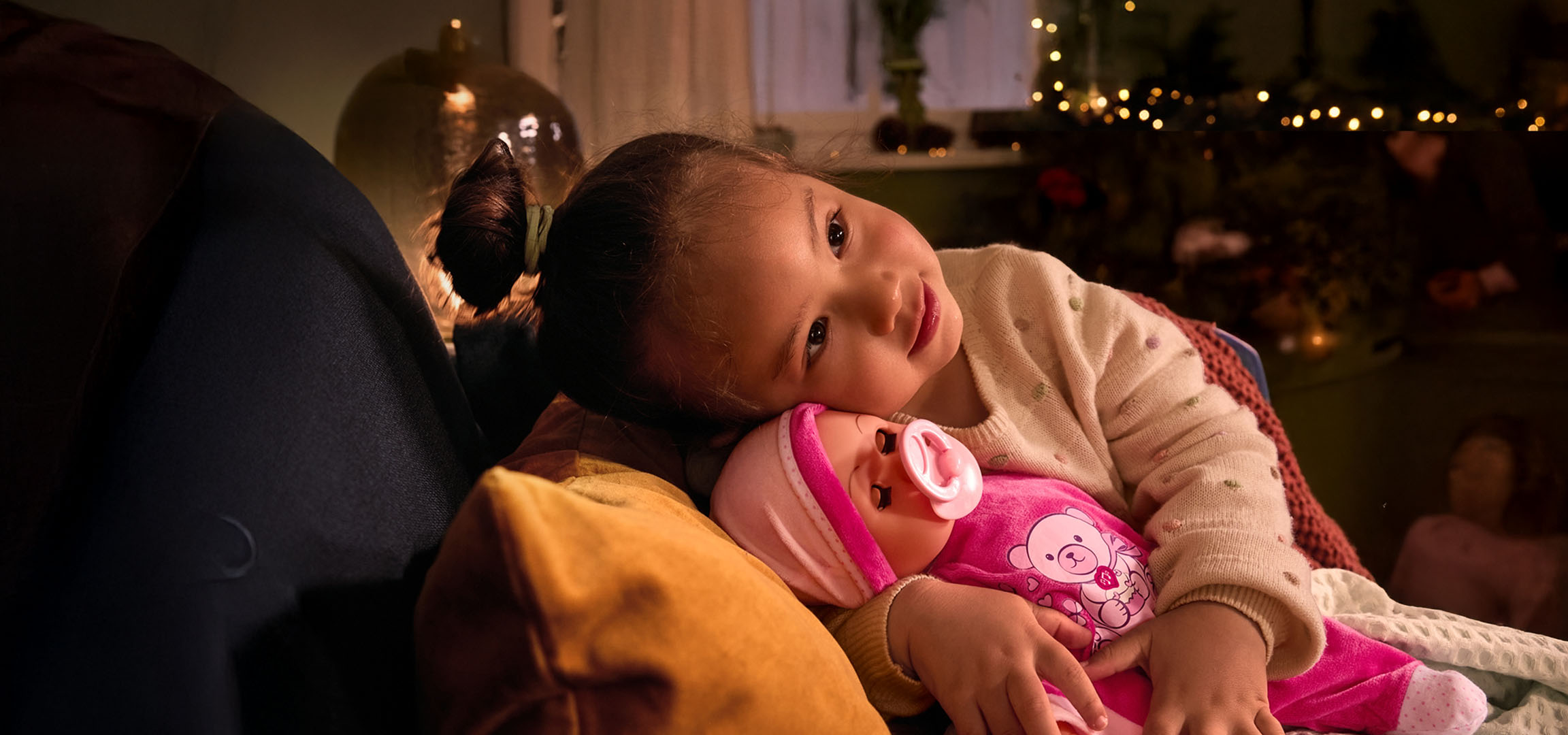 Κορίτσι με κούκλα και πιπίλα, άνετα τοποθετημένο σε μαξιλάρι.