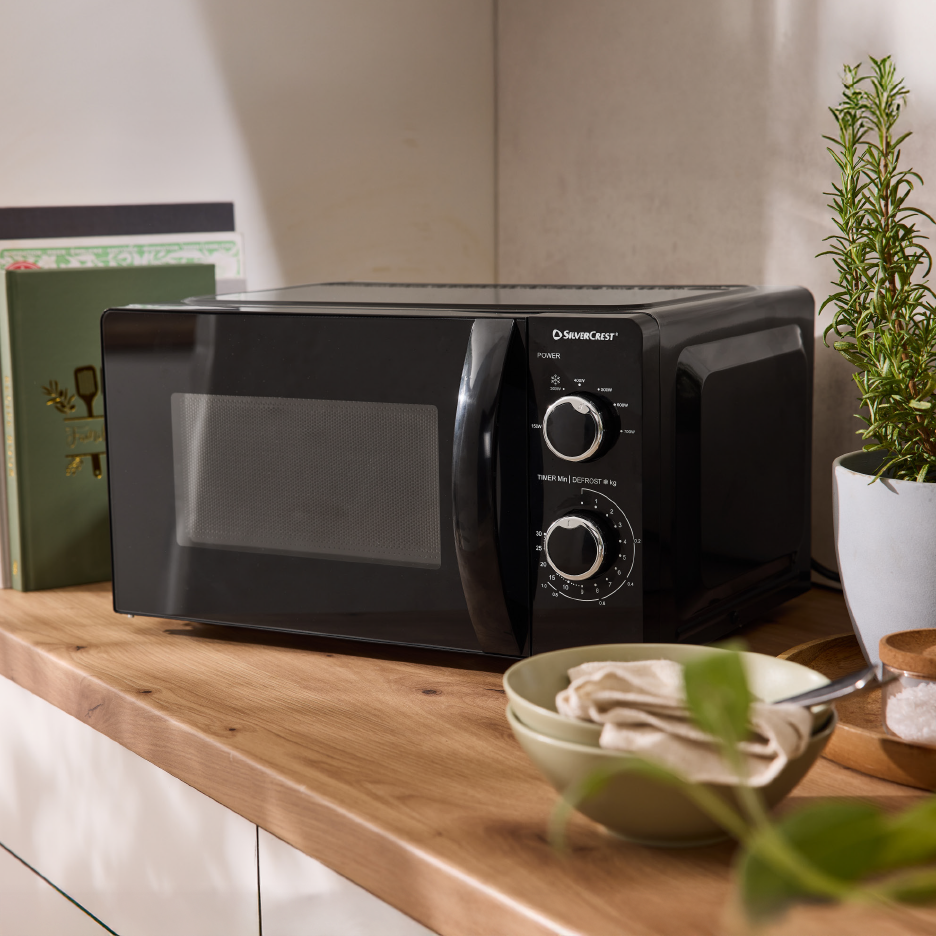 Μαύρος φούρνος μικροκυμάτων σε ξύλινο πάγκο κουζίνας με φυτά και μπολ.