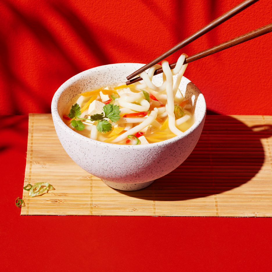 Μπολ με νουντλς, τόφου, λαχανικά και κόλιανδρο, με ξυλάκια να σηκώνουν νουντλς.