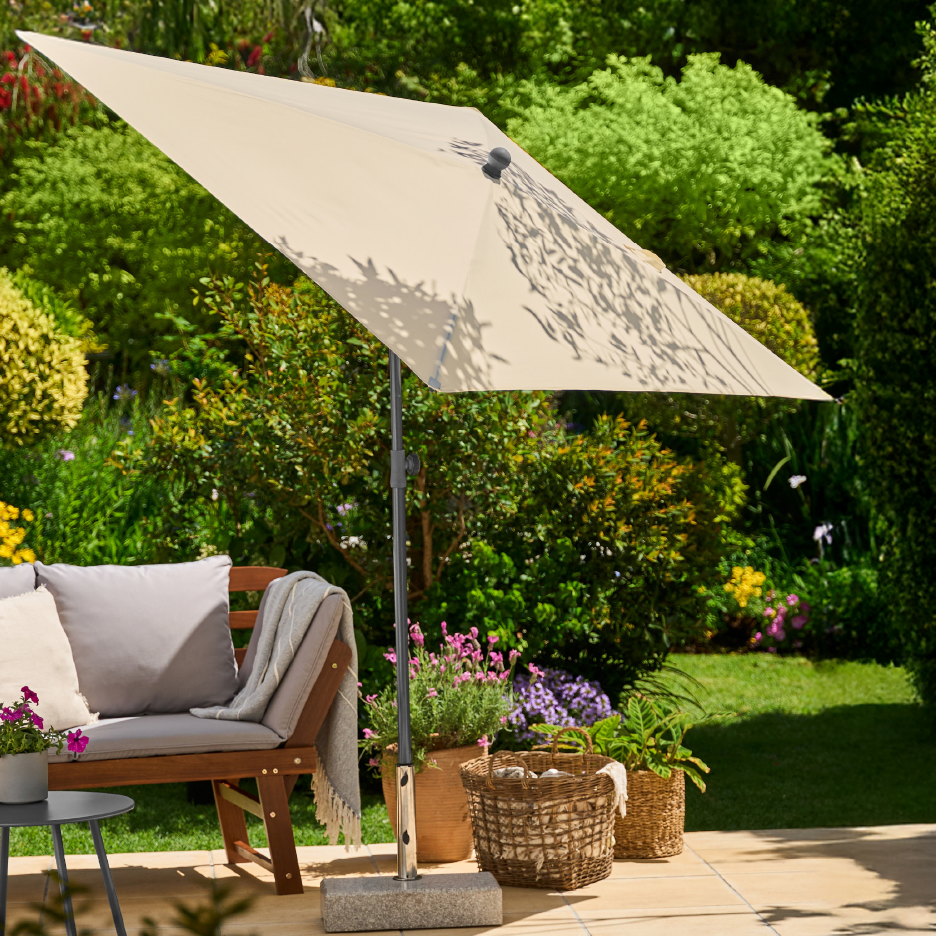 Ομπρέλα κήπου με βάση, παγκάκι με μαξιλάρια και καλάθια σε εξωτερικό χώρο.