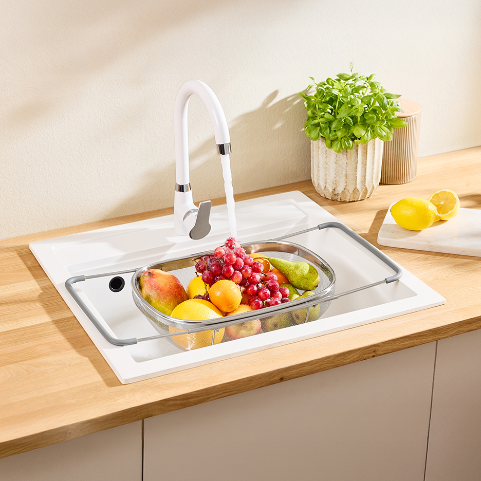 Νεροχύτης κουζίνας με βρύση, φρούτα σε σουρωτήρι και φυτό σε γλάστρα.