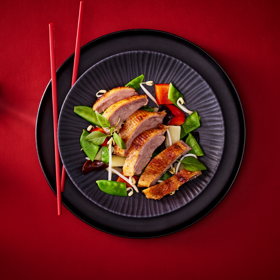 Πάπια με λαχανικά, φύτρες φασολιών και κόκκινες πιπεριές σε μαύρο πιάτο με ξυλάκια.