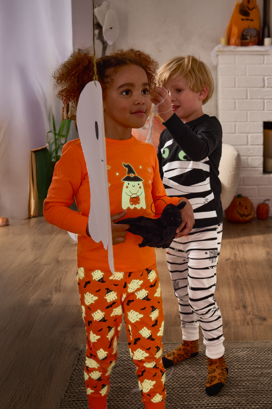 Παιδιά με πιτζάμες με θέμα το Halloween, το ένα κρατάει ένα παιχνίδι νυχτερίδα.