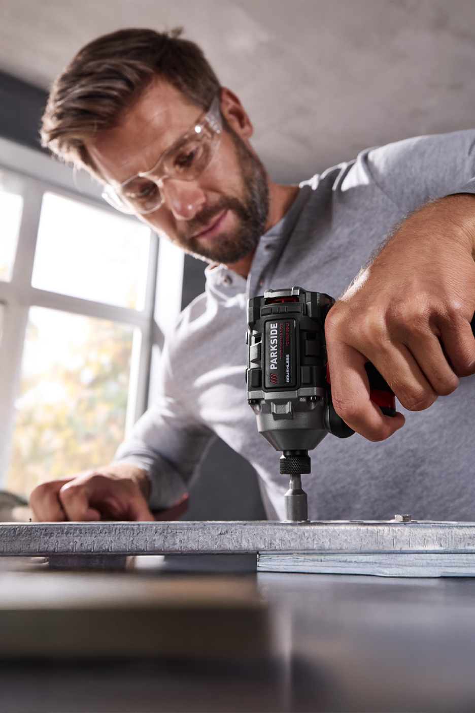 Άνδρας με γυαλιά ασφαλείας χρησιμοποιεί ένα κρουστικό κατσαβίδι Parkside Performance.