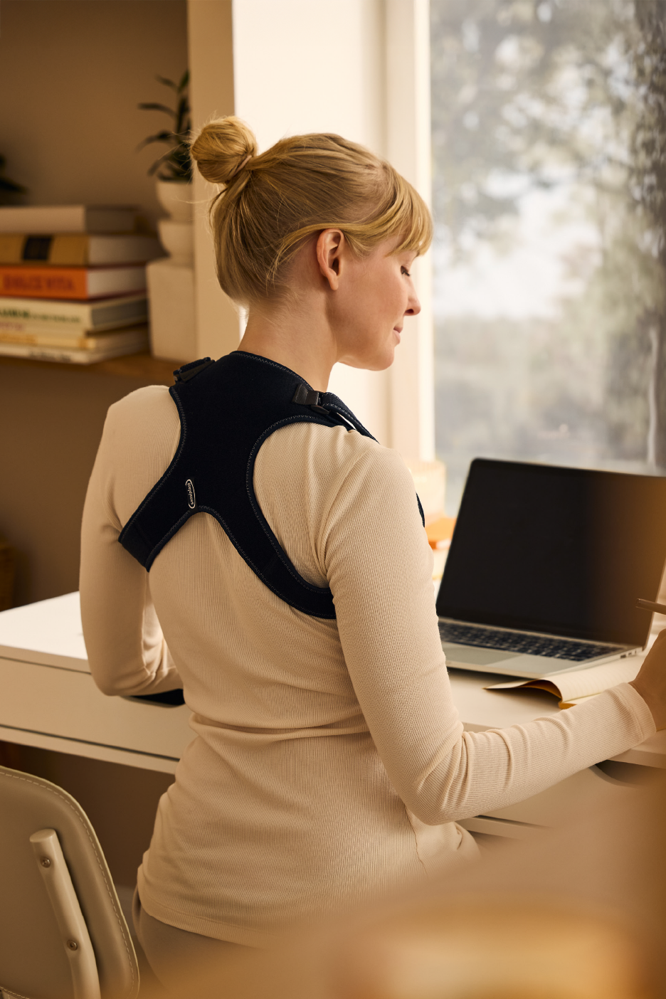 Γυναίκα με υποστηρικτικό σουτιέν πλάτης εργάζεται σε φορητό υπολογιστή σε ένα γραφείο.