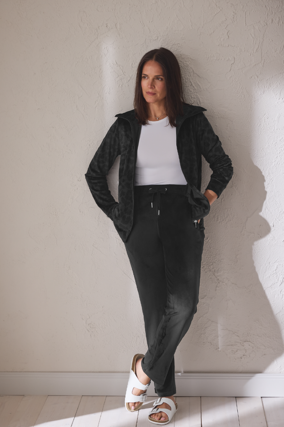 Γυναικεία βελουτέ ζακέτα και παντελόνι φόρμας σε μαύρο χρώμα, με λευκό τοπ και σανδάλια.