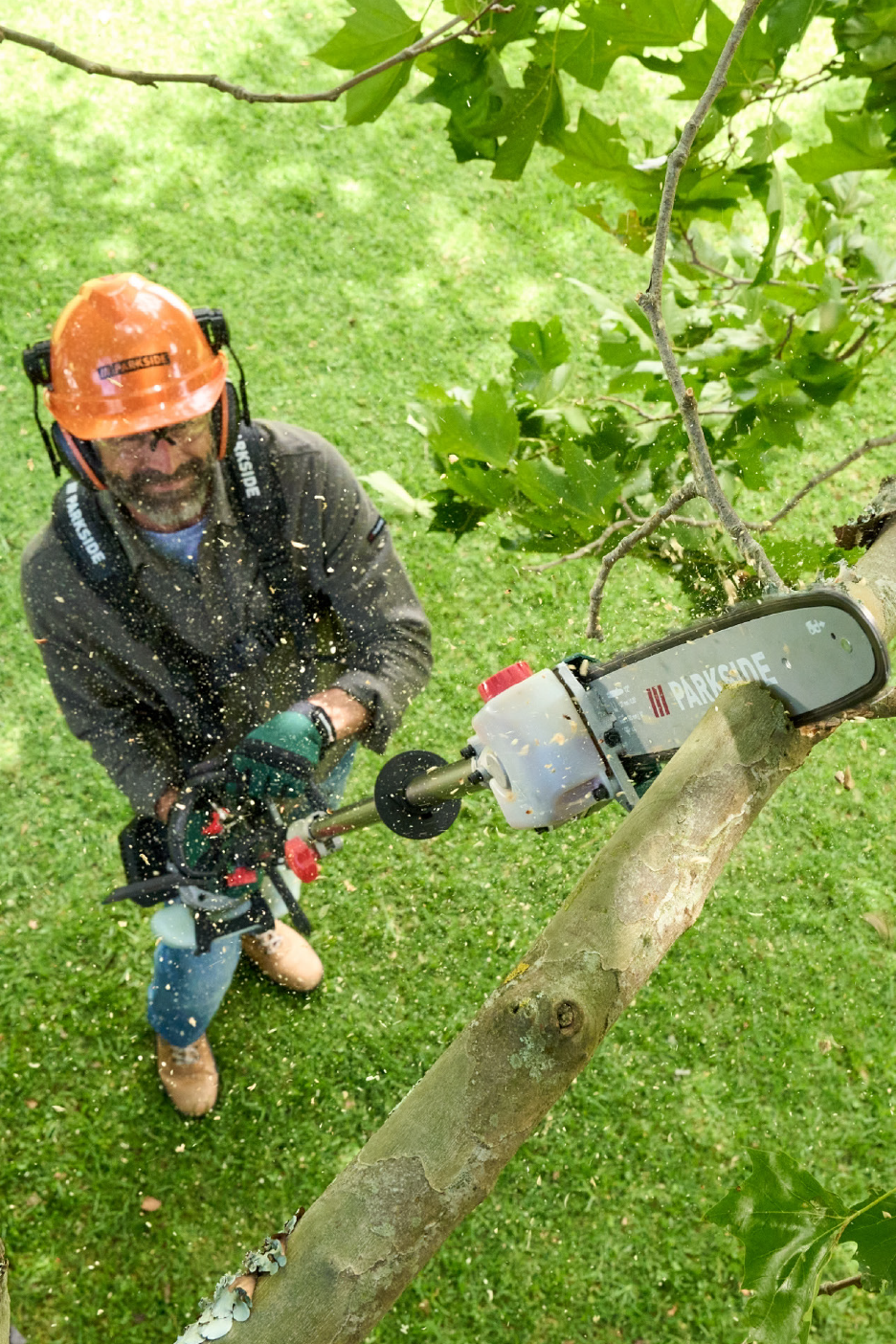 Άνδρας με κράνος ασφαλείας κλαδεύει δέντρο με αλυσοπρίονο κονταριού.