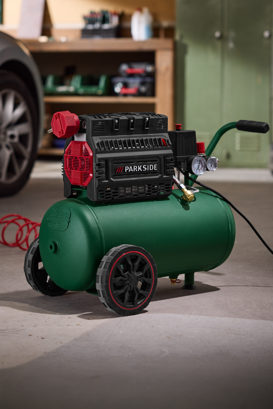 Πράσινος αεροσυμπιεστής με τροχούς και κόκκινες λεπτομέρειες σε γκαράζ.