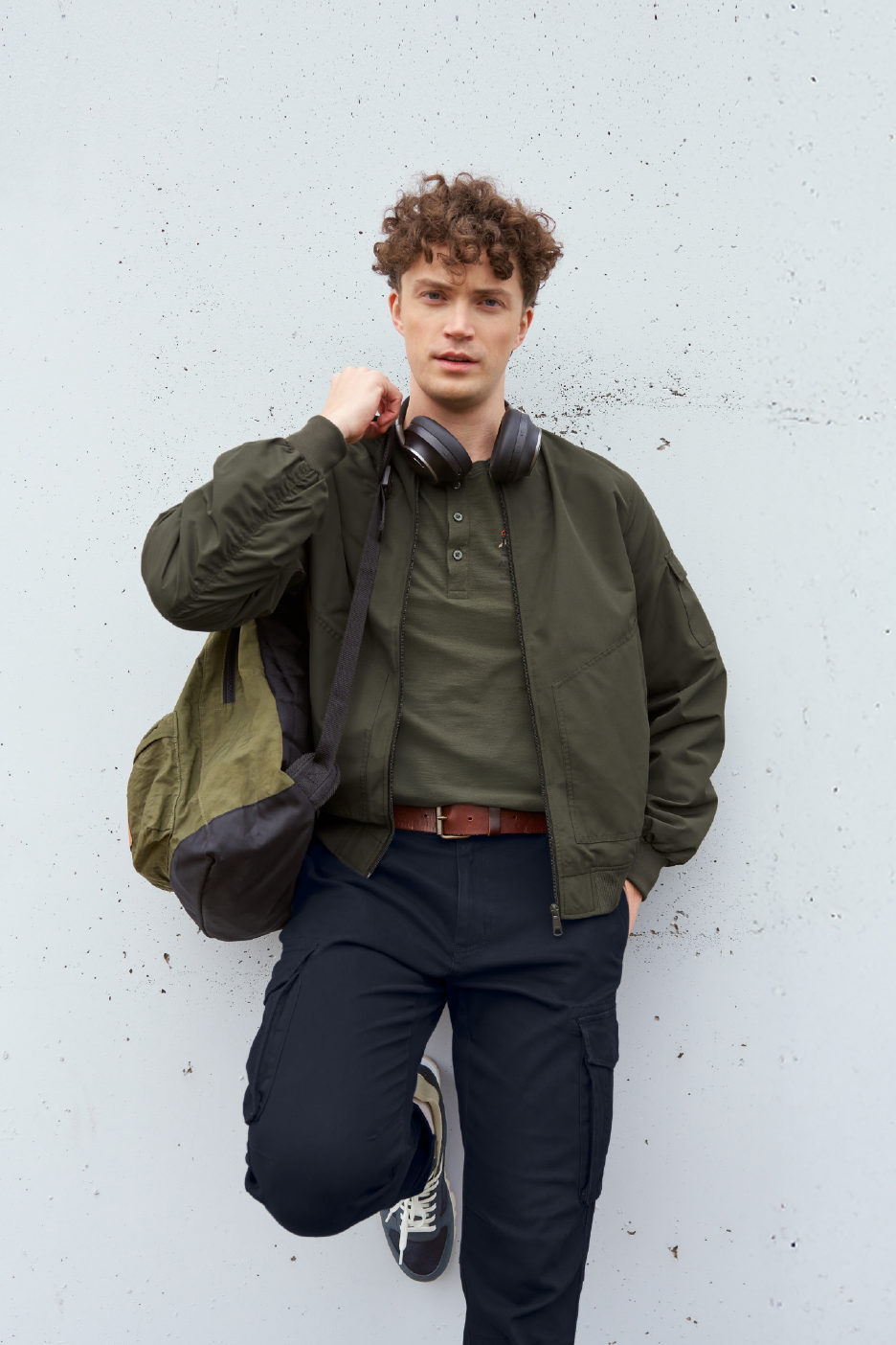 Άνδρας με χακί μπουφάν, μπλουζάκι πόλο, σκούρο μπλε παντελόνι cargo και ακουστικά.