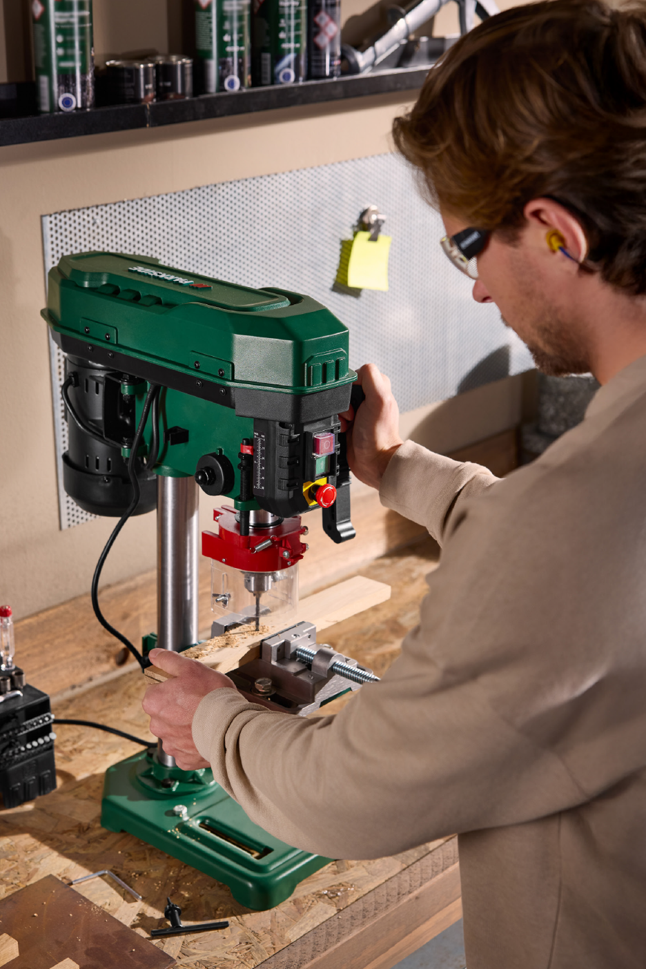 Άνδρας χρησιμοποιεί ένα επιτραπέζιο δράπανο για να τρυπήσει ένα ξύλινο κομμάτι.