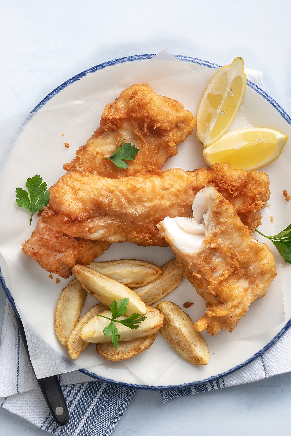 Τραγανό ψάρι με πατάτες τηγανητές και φέτες λεμονιού σε λευκό πιάτο.