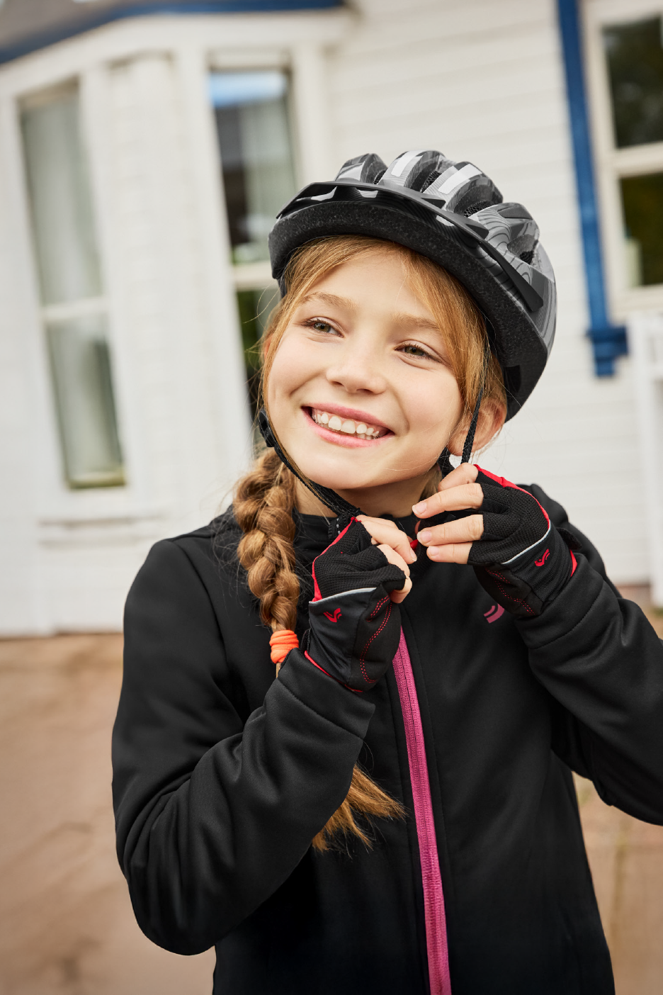 Χαμογελαστό κορίτσι με μαύρο κράνος ποδηλάτου, μαύρο μπουφάν και γάντια ποδηλασίας.
