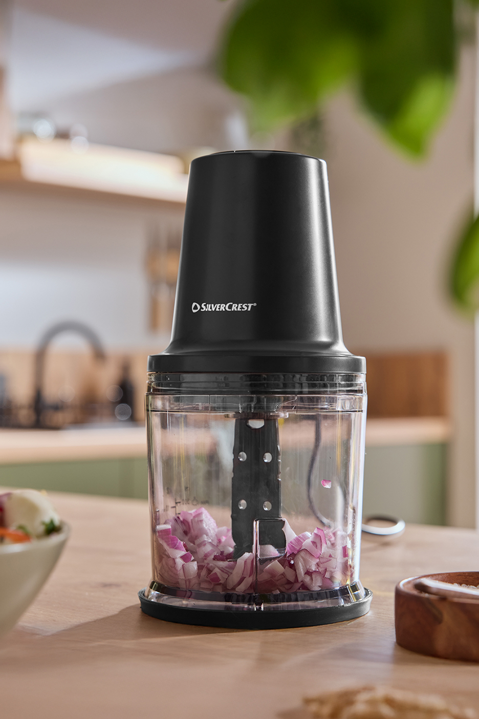 Μαύρος μίνι κόφτης με ψιλοκομμένο κρεμμύδι σε ξύλινο πάγκο κουζίνας.