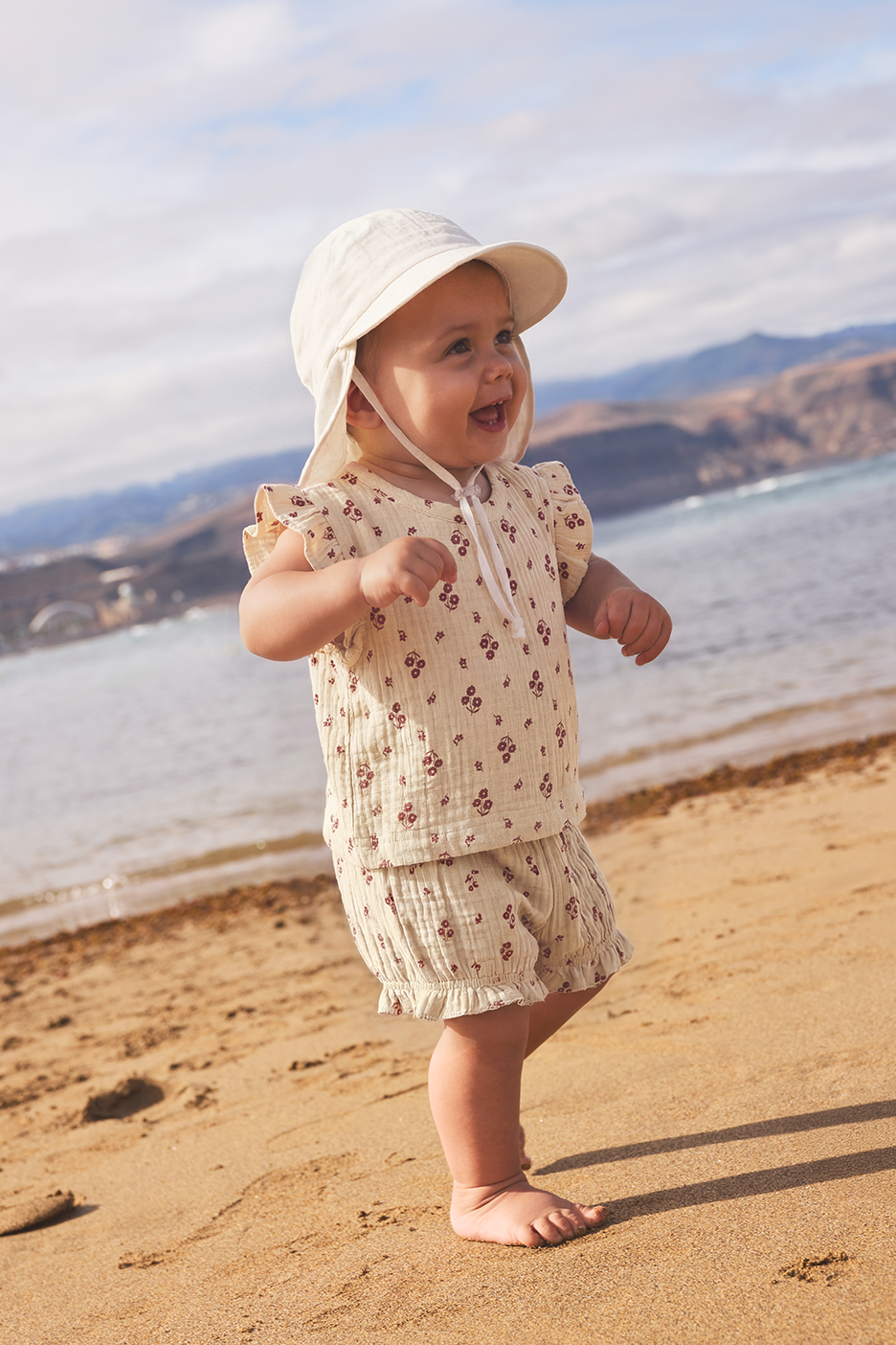 Χαρούμενο μωρό με καπέλο και σετ ρούχων με λουλούδια στην παραλία.