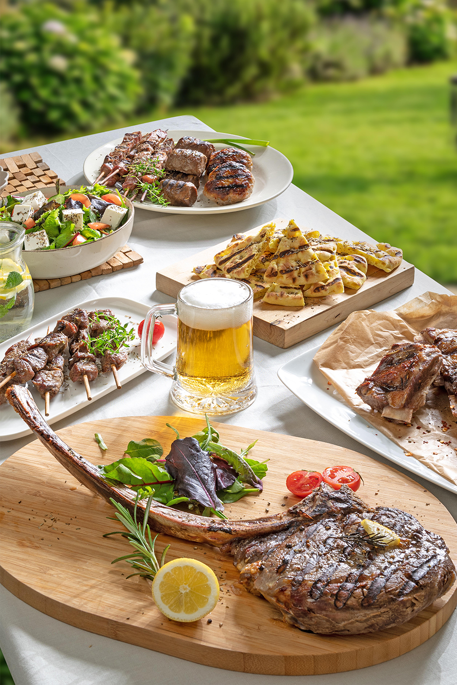 Μια ποικιλία από ψητά κρέατα, σαλάτα, ψωμί και μπύρα σε ένα τραπέζι εξωτερικού χώρου.