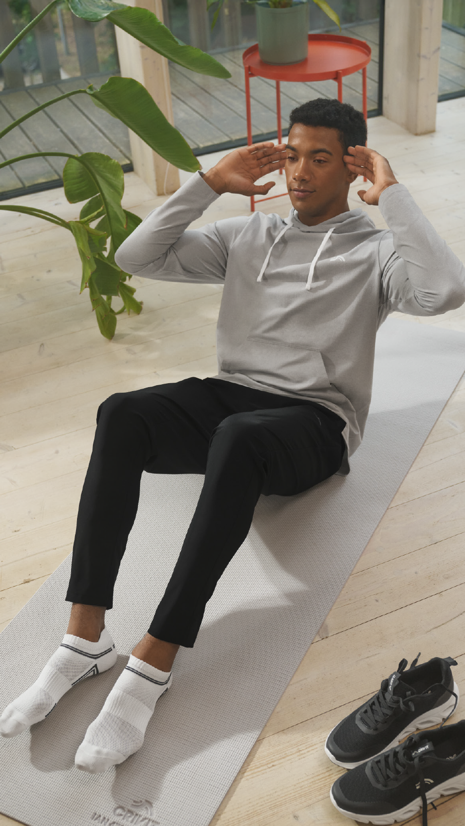 Άντρας με γκρι φούτερ και μαύρο παντελόνι κάνει κοιλιακούς σε χαλάκι γιόγκα.