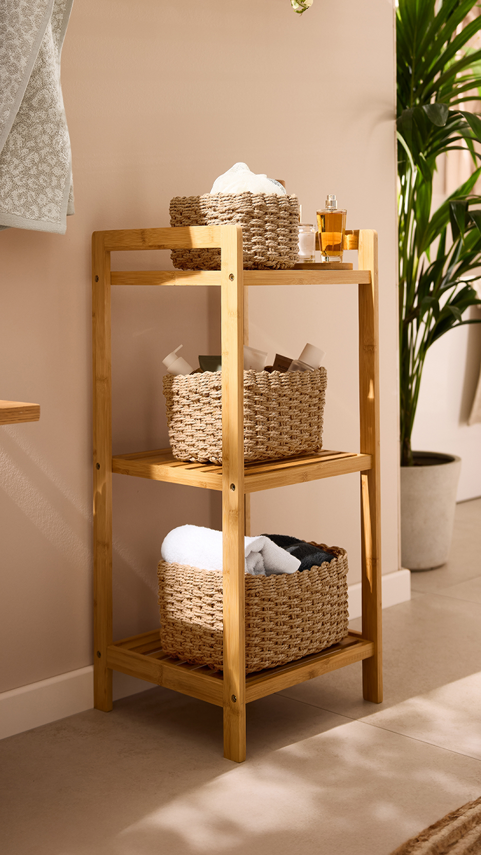 Ξύλινη ραφιέρα μπάνιου με ψάθινα καλάθια, πετσέτες και προϊόντα περιποίησης.
