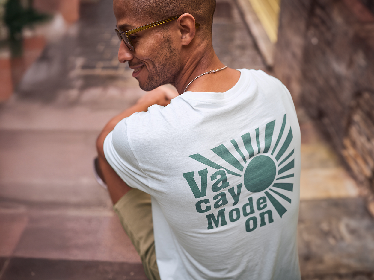 Ένας άντρας φοράει ένα λευκό t-shirt με την επιγραφή 'Vacay Mode On' και χαμογελάει.