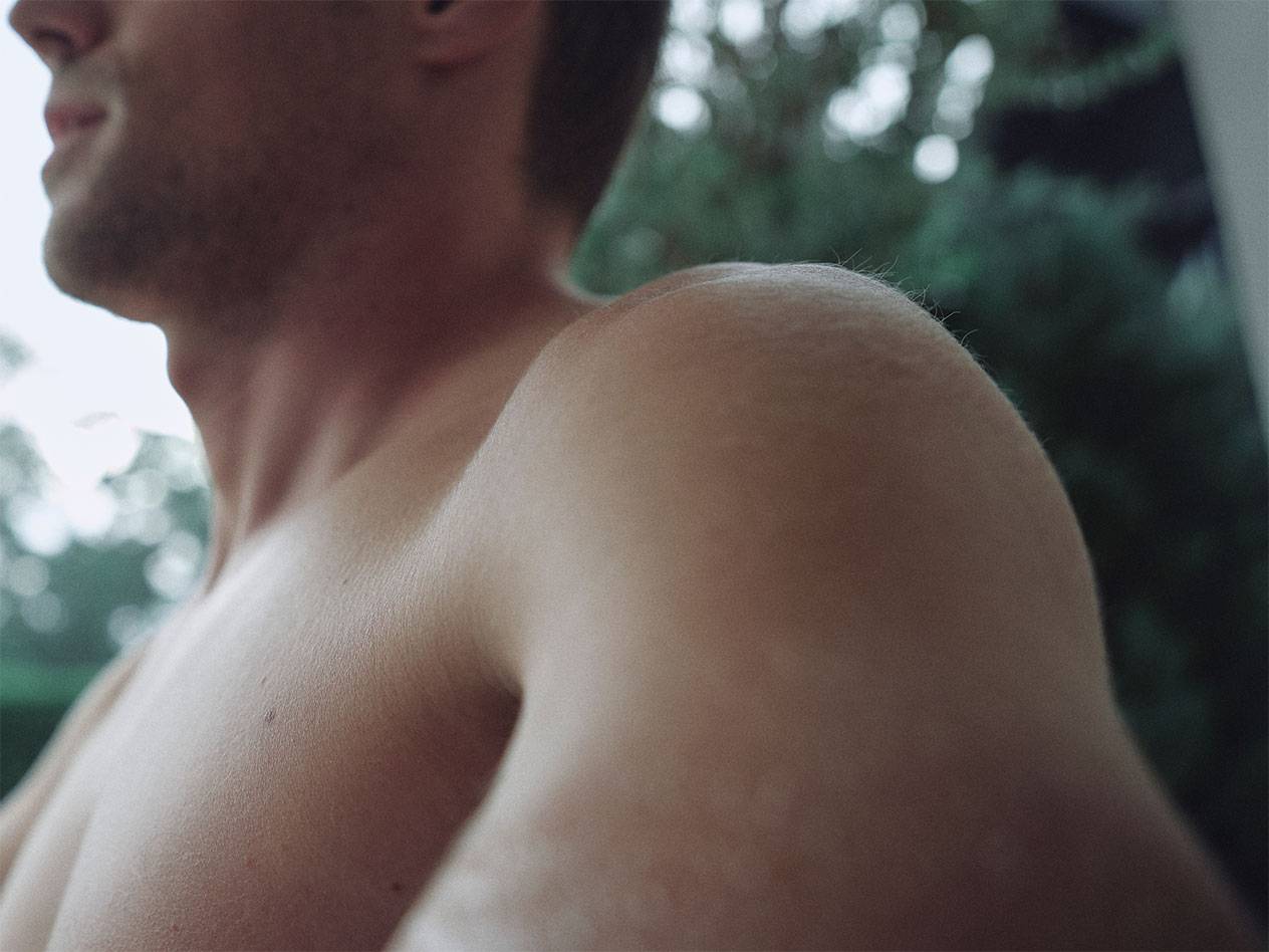 Κοντινό πλάνο ώμου και λαιμού άνδρα, με θολό πράσινο φόντο.