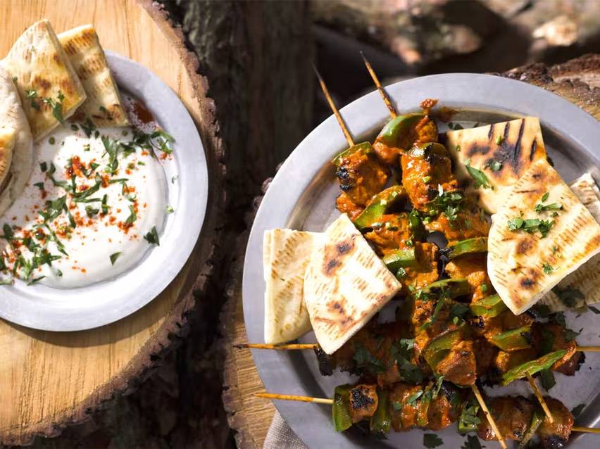 Σουβλάκια κοτόπουλου με πιπεριές, πίτες και ντιπ γιαουρτιού σε ξύλινη επιφάνεια.