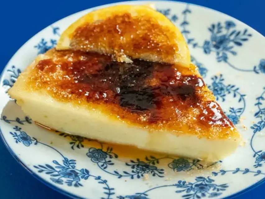 Φέτα κρεμώδους επιδορπίου με καραμελωμένη ζάχαρη και φέτα πορτοκαλιού σε μπλε και λευκό πιάτο.