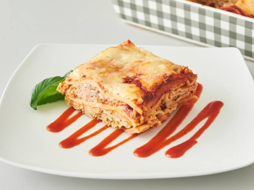 Μια μερίδα λαζάνια με σάλτσα ντομάτας και φύλλα βασιλικού σε ένα λευκό πιάτο.