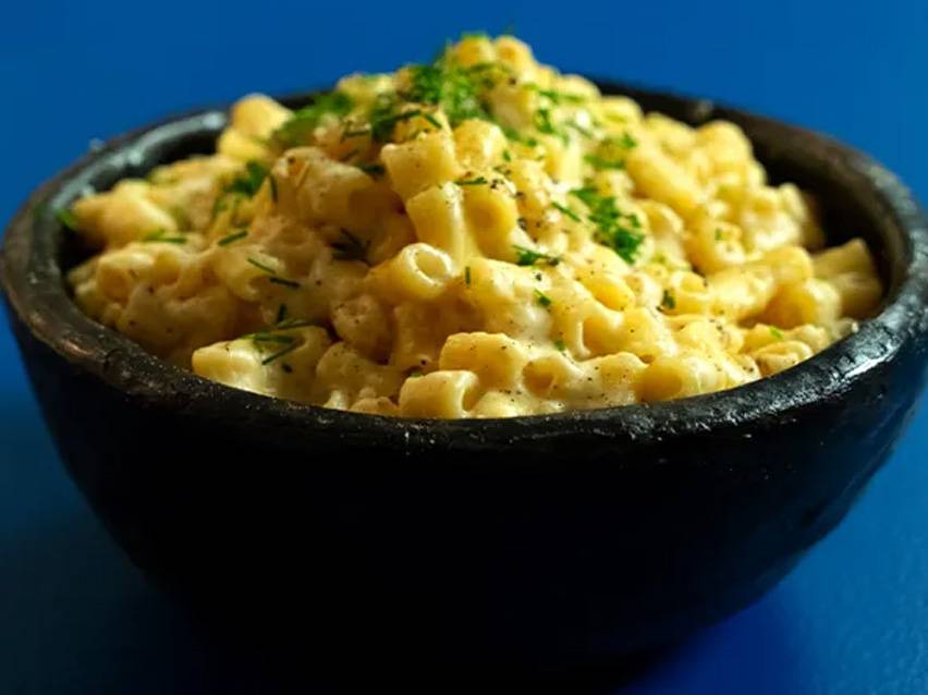 Μακαρόνια με τυρί σε μαύρο μπολ, πασπαλισμένα με φρέσκα μυρωδικά.