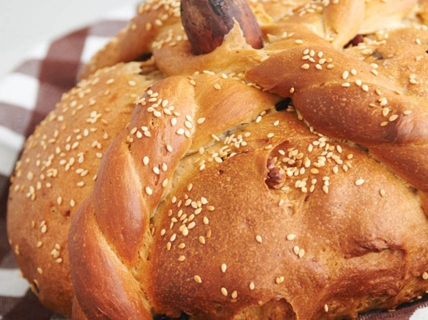 Ψωμί σε σχήμα κολοκύθας με σουσάμι και πλεξούδες, πάνω σε καρό ύφασμα.