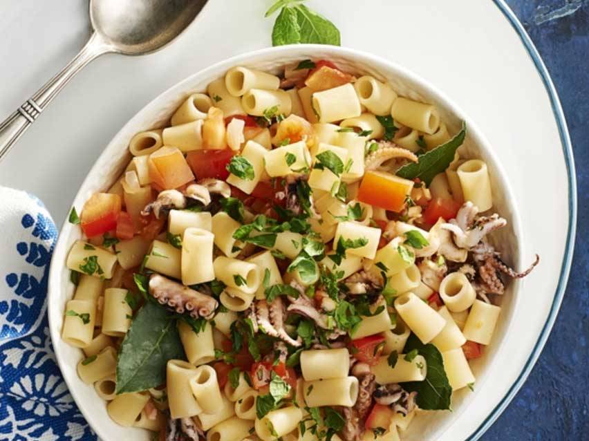 Μακαρόνια με χταπόδι, ντομάτα και μαϊντανό σε λευκό μπολ.