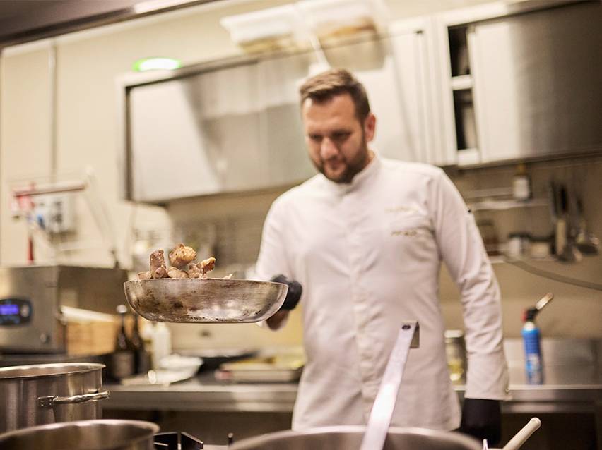 Σεφ με λευκή ποδιά πετάει φαγητό σε τηγάνι.