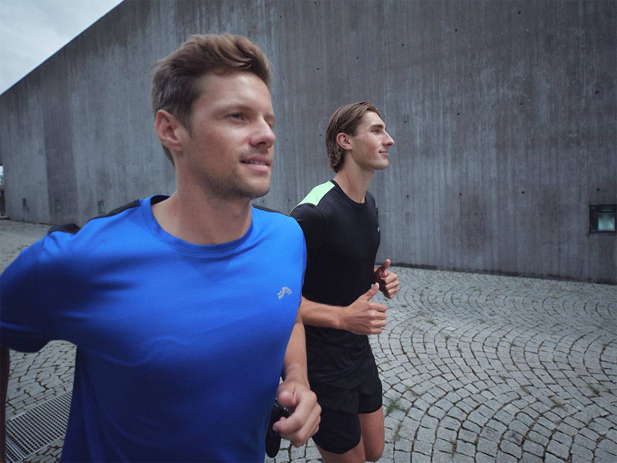 Δύο άνδρες τρέχουν με αθλητικά μπλουζάκια και σορτς, ένας μπλε και ένας μαύρος.