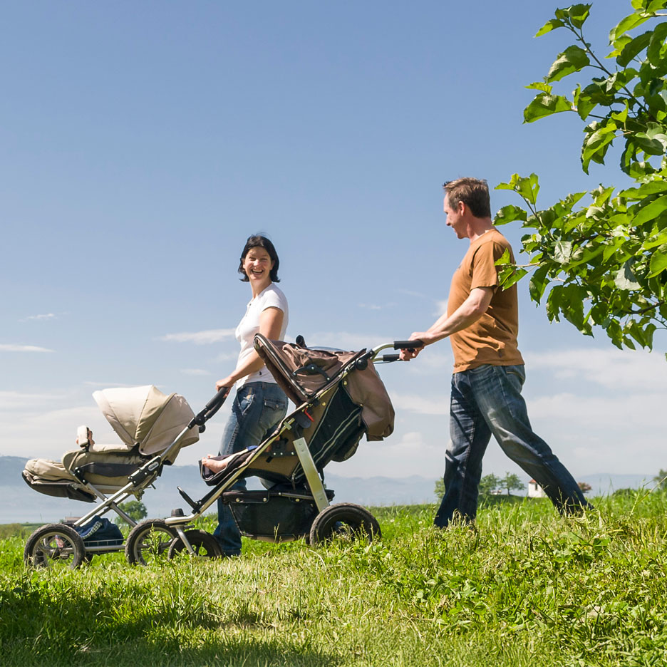 Uma família passeia num prado com um carrinho de bebé.