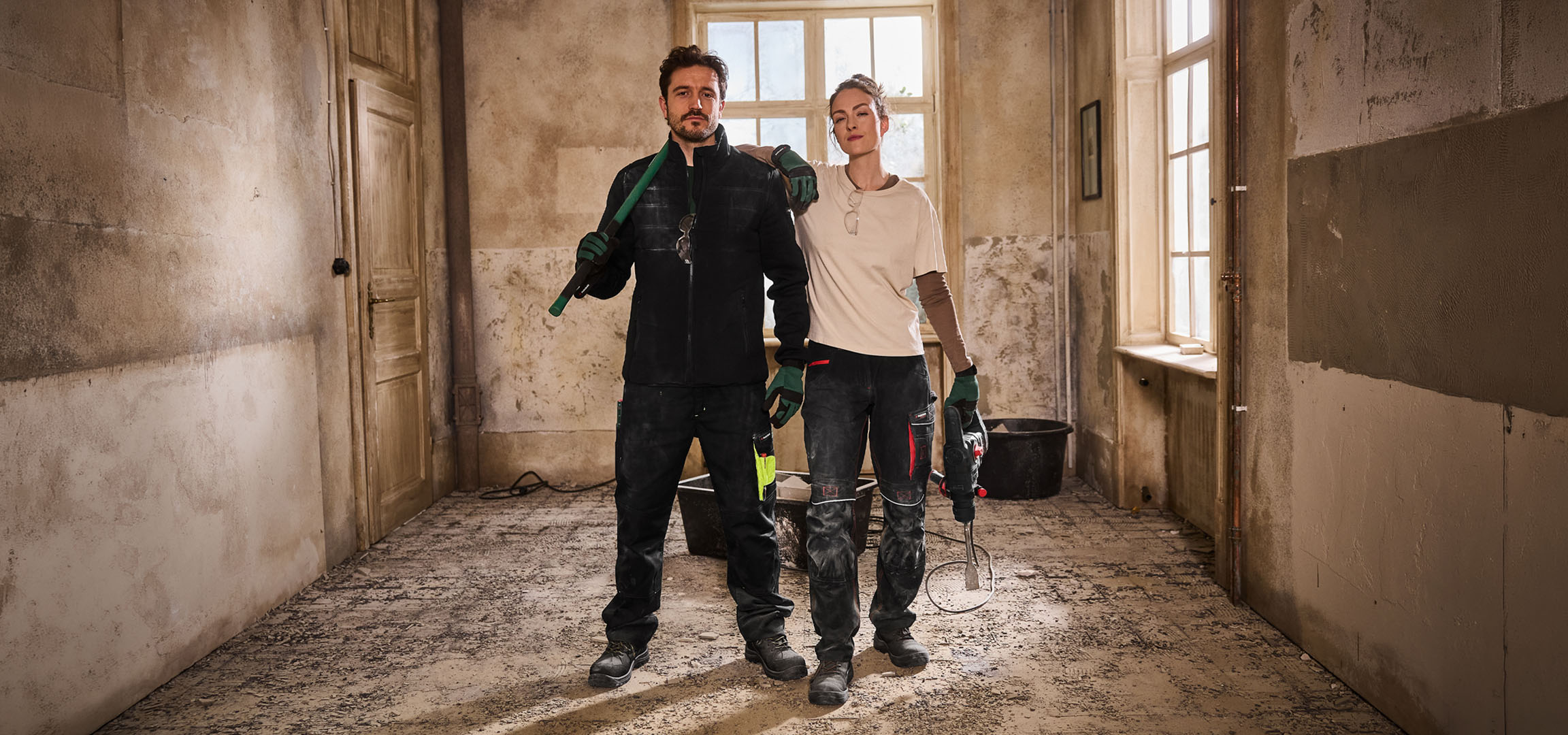 Δύο εργάτες οικοδομών με ρούχα εργασίας και εργαλεία σε εργοτάξιο.