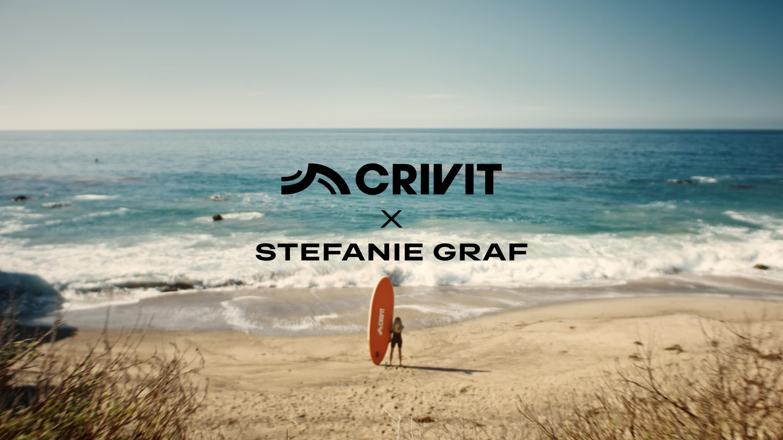 Γυναίκα με πορτοκαλί σανίδα SUP σε αμμώδη παραλία, με τη θάλασσα στο βάθος.