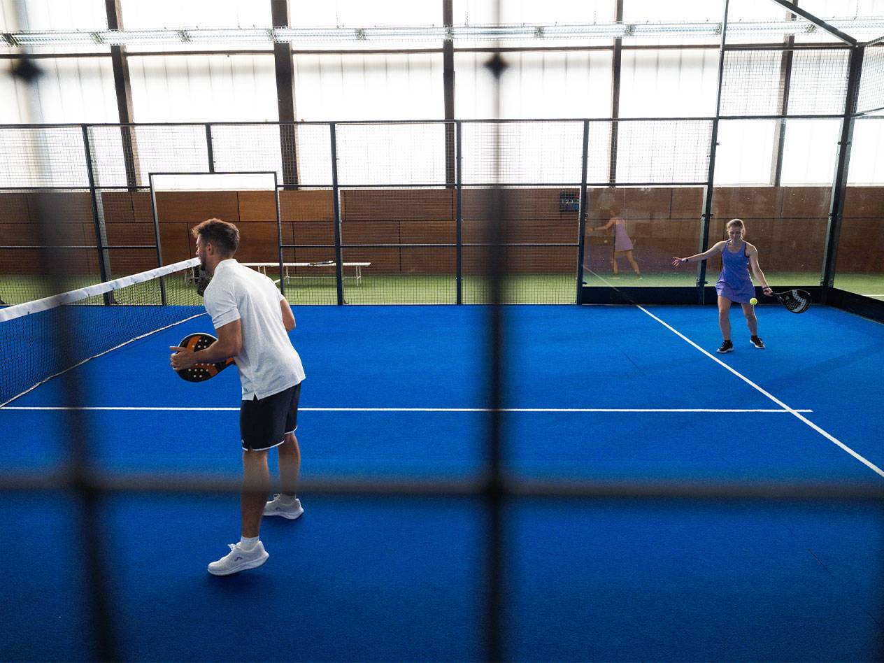 Άνδρας και γυναίκα παίζουν padel σε μπλε γήπεδο με ρακέτες και μπάλα.
