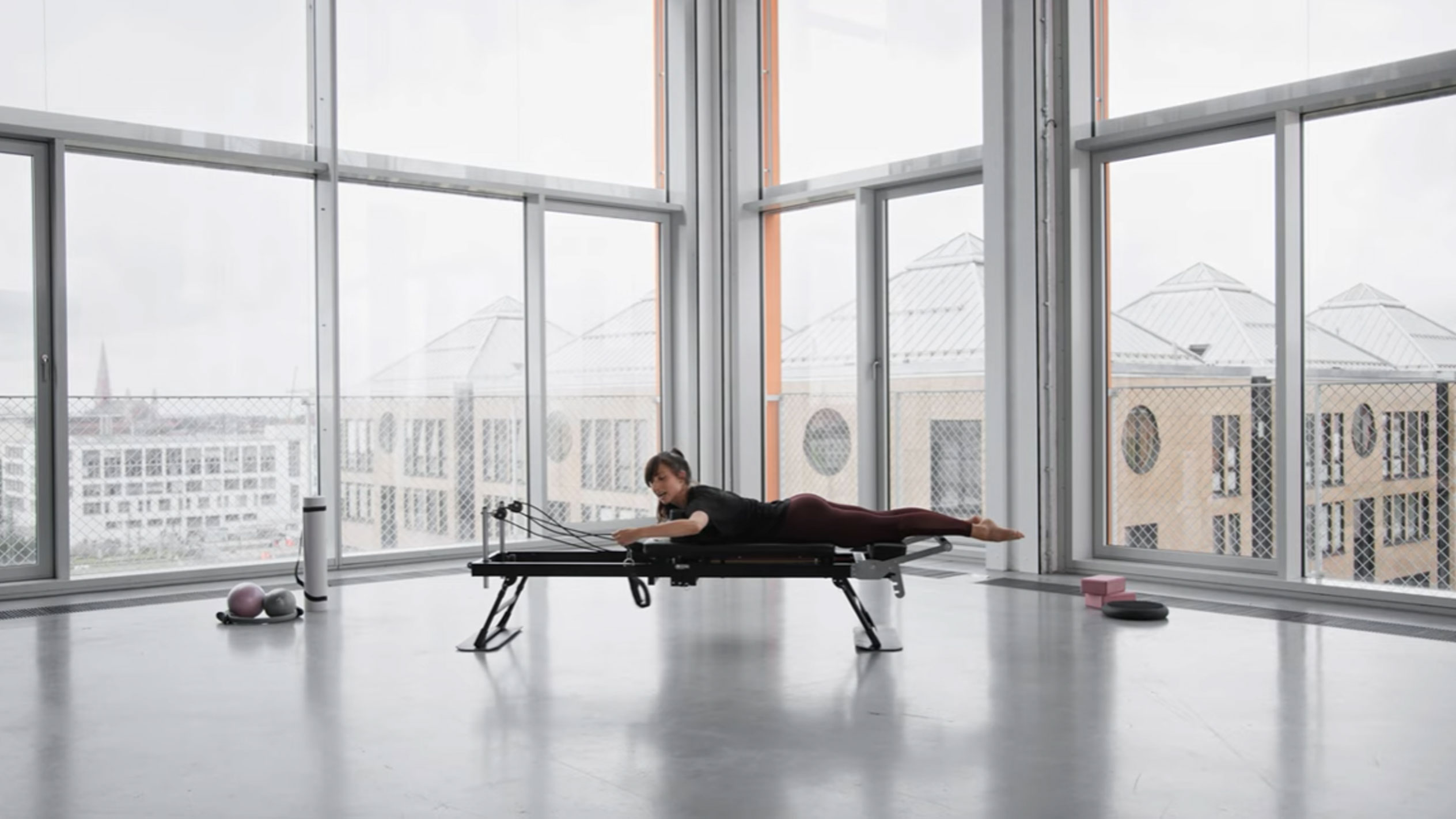 Γυναίκα κάνει Pilates σε reformer, με θέα στην πόλη.